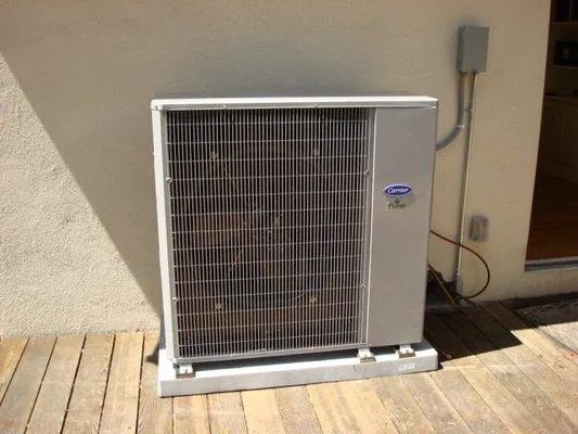 Air conditioning unit on a wooden deck next to a building wall with electrical wiring visible.