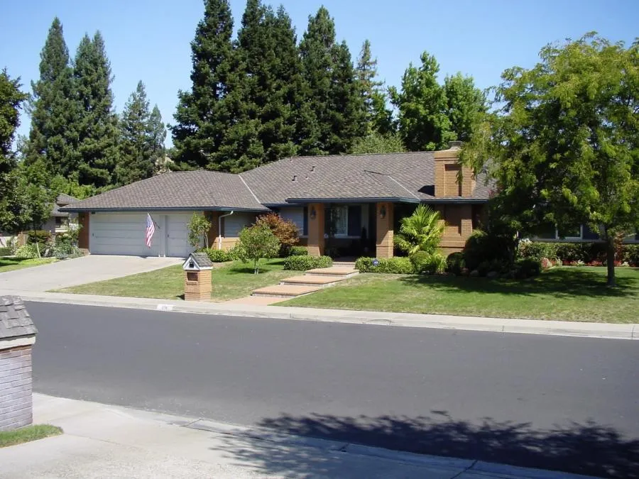 Suburban home with a well-maintained roof, surrounded by landscaped greenery, under a clear sky.