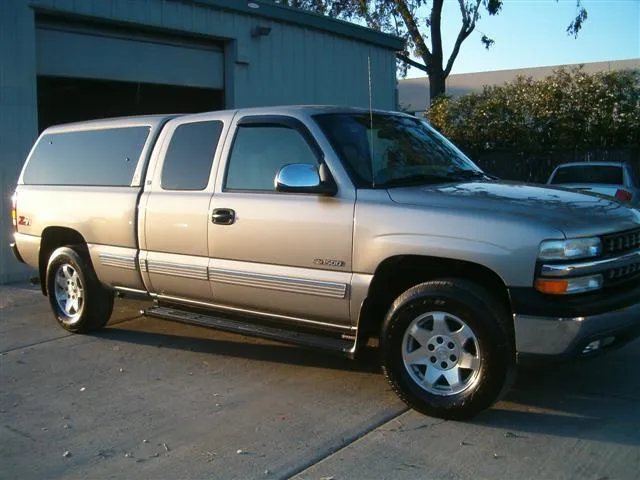  A freshly polished beige pickup truck with a camper shell parked outside a workshop.