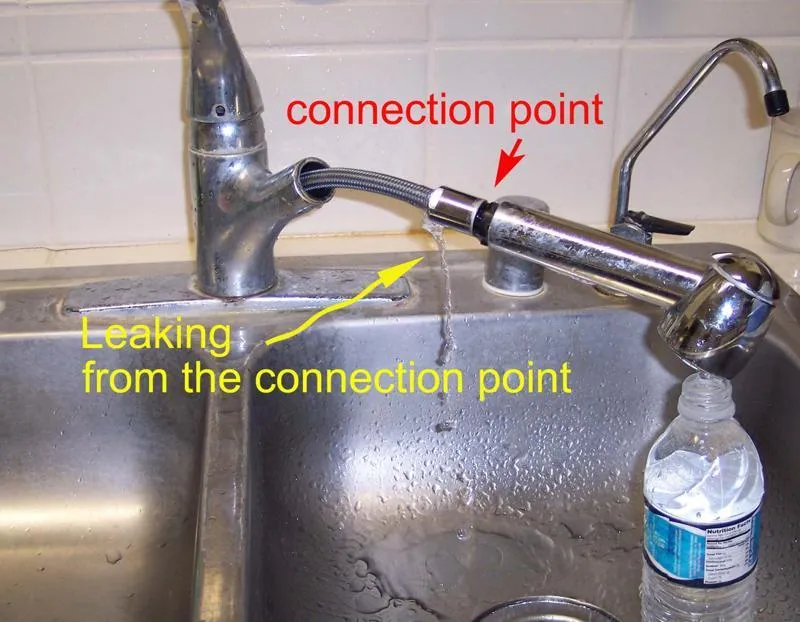Kitchen faucet with leak at connection point, water dripping into sink, plastic bottle nearby.