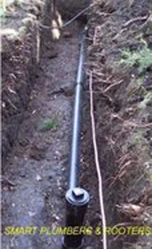  A long black pipe is installed in a narrow trench surrounded by soil and grass.