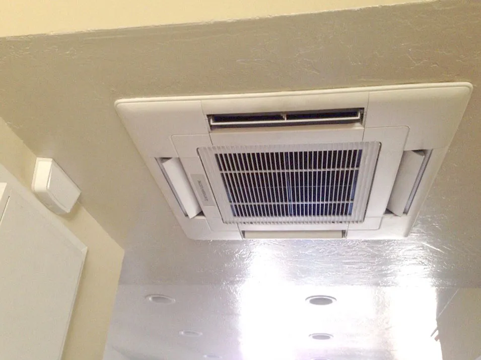 Ceiling-mounted air conditioning unit neatly installed in a white ceiling. Circular recessed lights surround the unit. Ceiling-mounted air conditioning unit neatly installed in a white ceiling. Circular recessed lights surround the unit.
