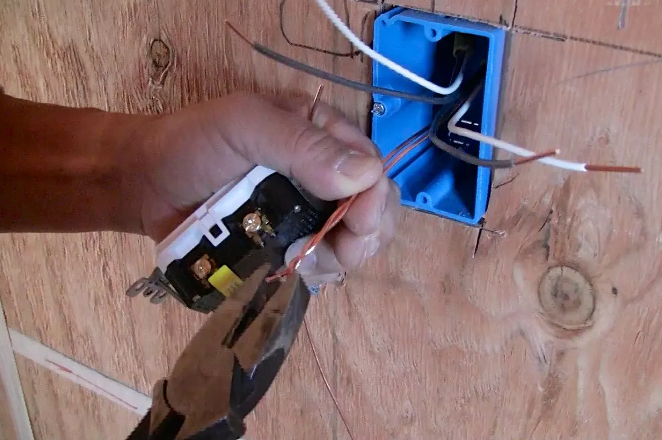 Hand using pliers to connect wires in a blue electrical box on a wooden wall. Hand using pliers to connect wires in a blue electrical box on a wooden wall.