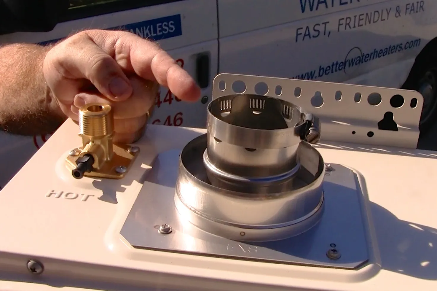 Close-up of a technician's hand pointing at connectors on a water heater installation with a company van in the background. Close-up of a technician's hand pointing at connectors on a water heater installation with a company van in the background.
