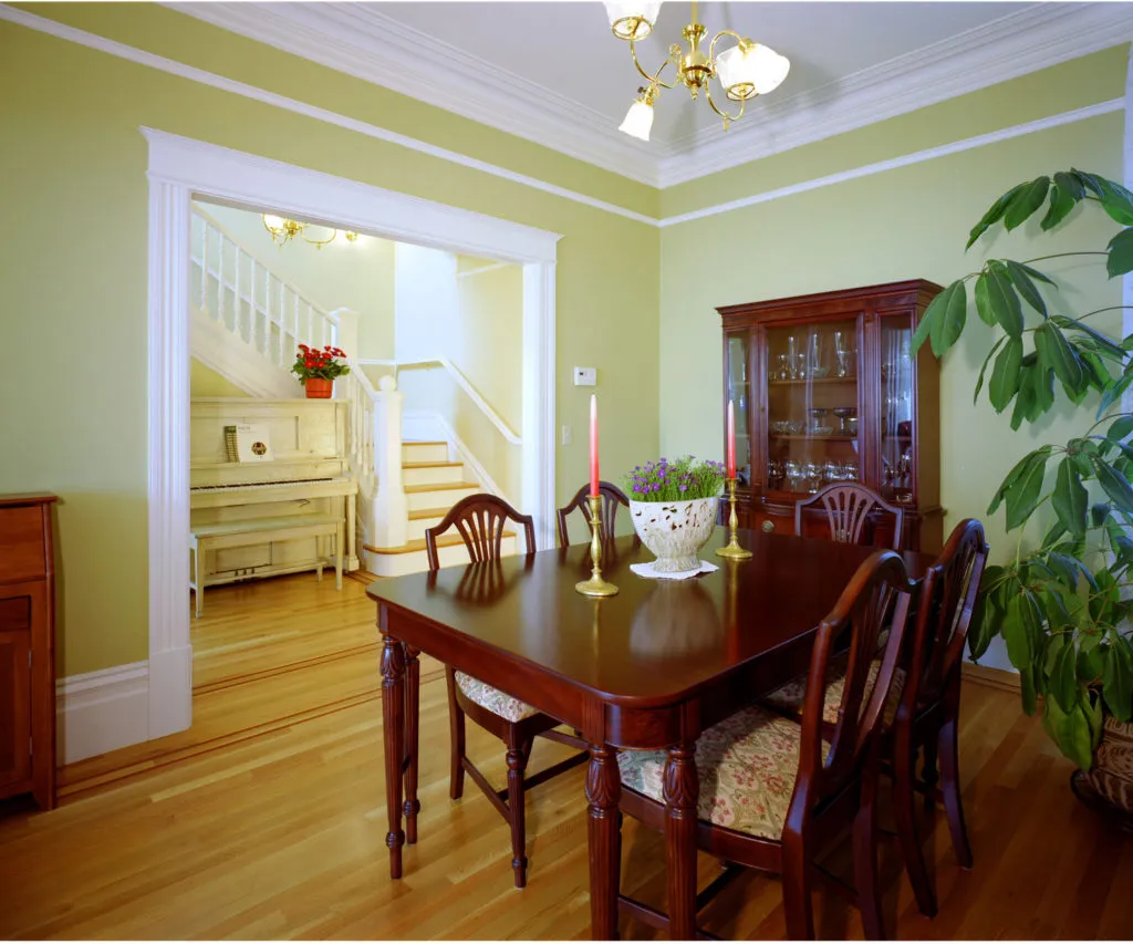  Dining room with wooden furniture, green walls, a staircase, and a white piano.