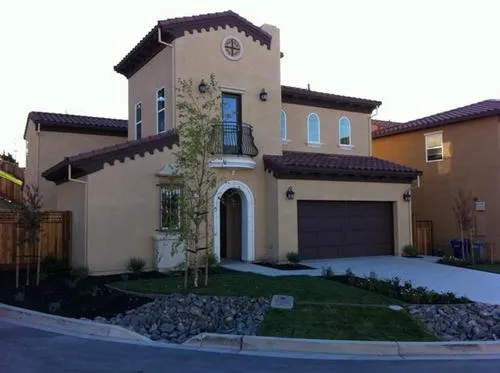 A two-story beige stucco house with a tile roof, arched doorway, and well-maintained landscaping in the front yard. A two-story beige stucco house with a tile roof, arched doorway, and well-maintained landscaping in the front yard.