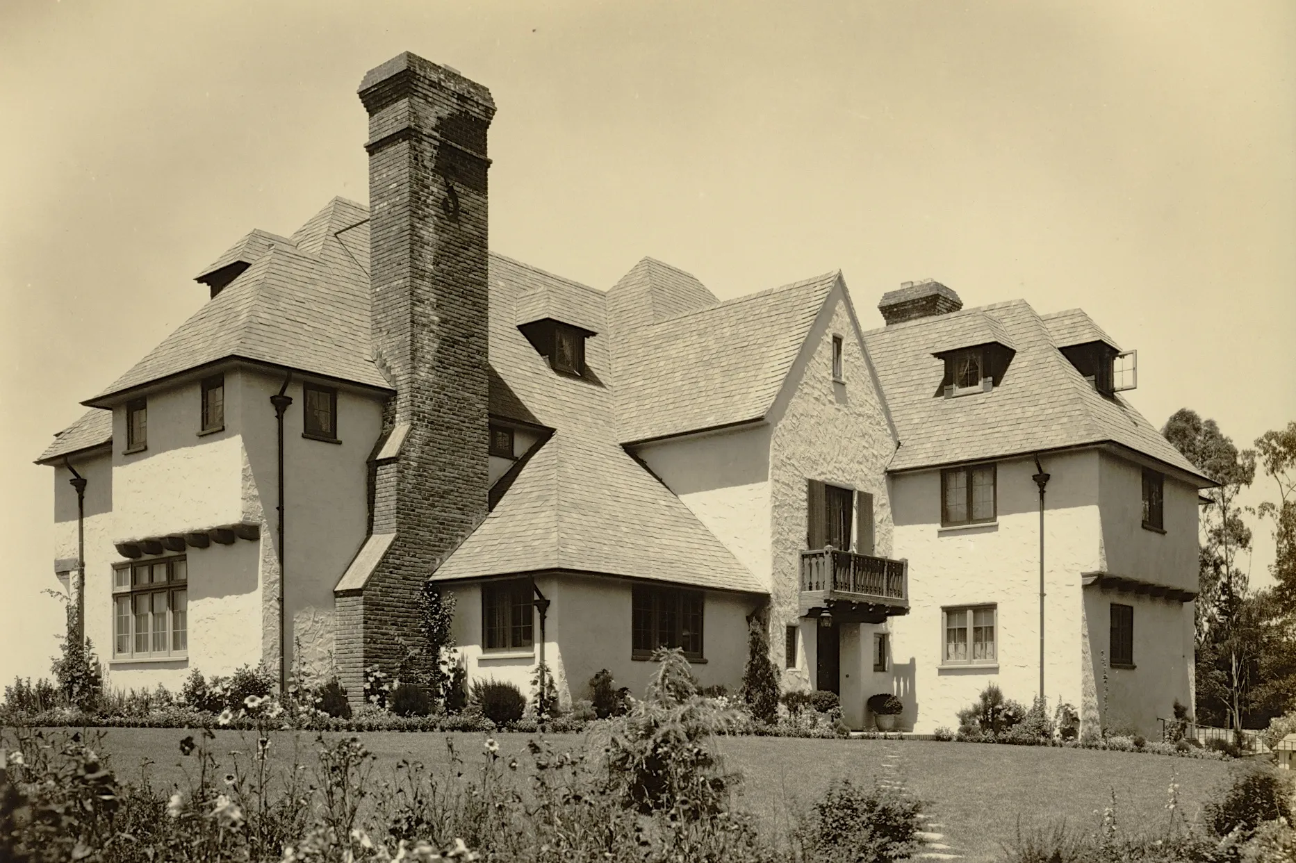 A historic house with steep roofs, multiple gables, and a prominent brick chimney, surrounded by a landscaped garden. A historic house with steep roofs, multiple gables, and a prominent brick chimney, surrounded by a landscaped garden.