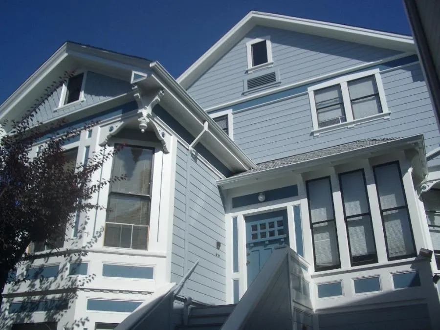  A light blue house with white trim, showcasing detailed window and door frames, set against a clear blue sky.