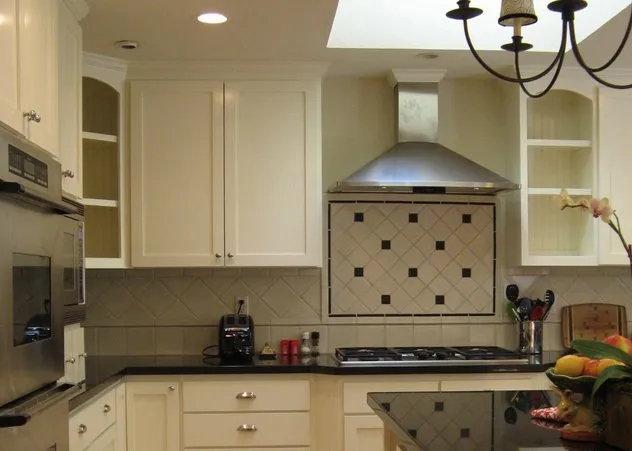 Modern kitchen with white cabinets, black countertops, a stainless steel oven and range hood, and a fruit basket on the island. Modern kitchen with white cabinets, black countertops, a stainless steel oven and range hood, and a fruit basket on the island.