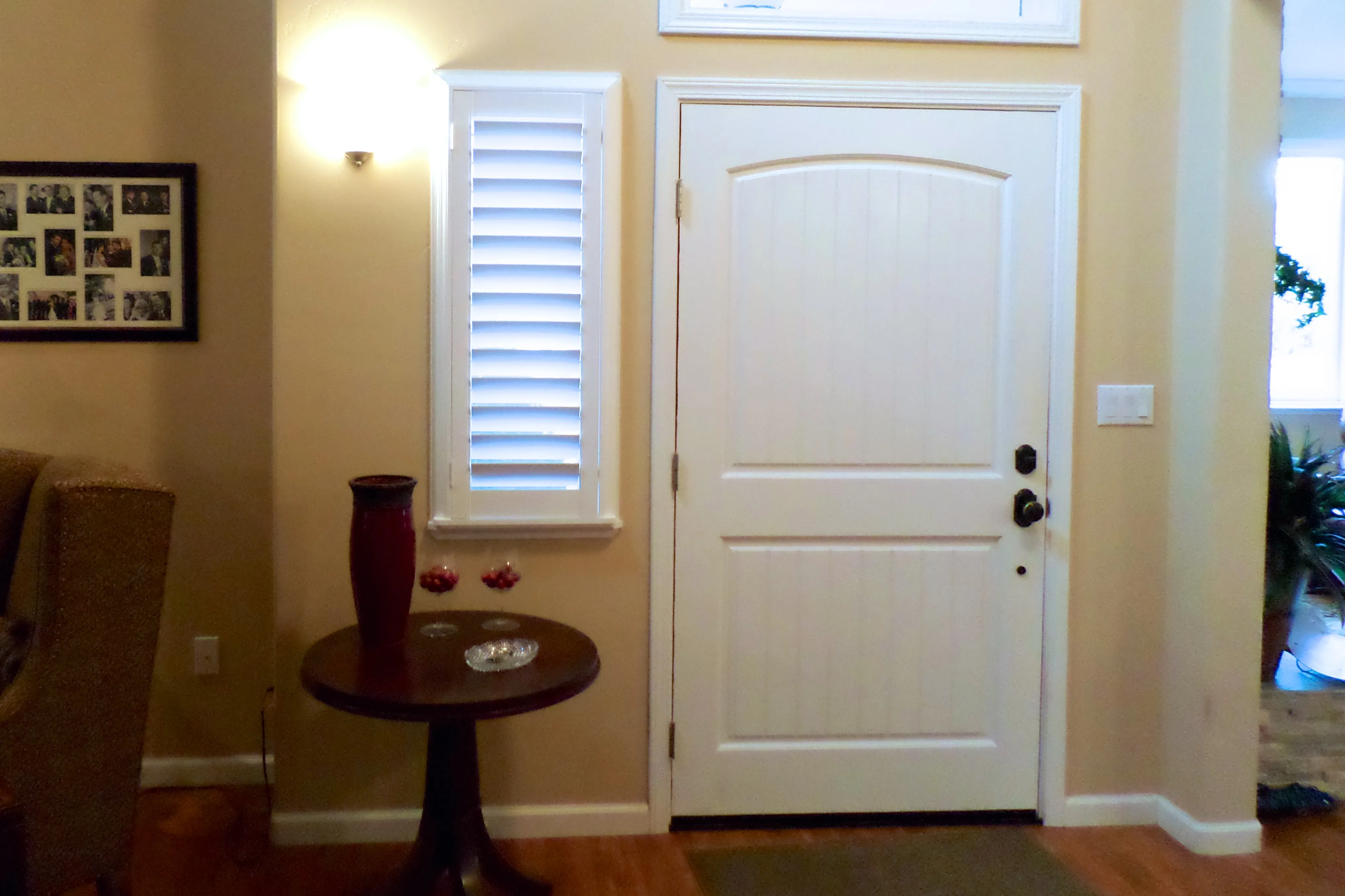 Interior view of a clean entryway with a white door, shutters, a small table, and a wall light. Interior view of a clean entryway with a white door, shutters, a small table, and a wall light.