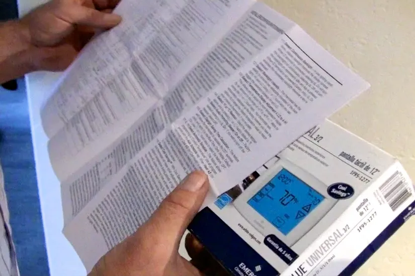 Hands holding a digital thermostat box and an open manual, focused on installation instructions. Hands holding a digital thermostat box and an open manual, focused on installation instructions.