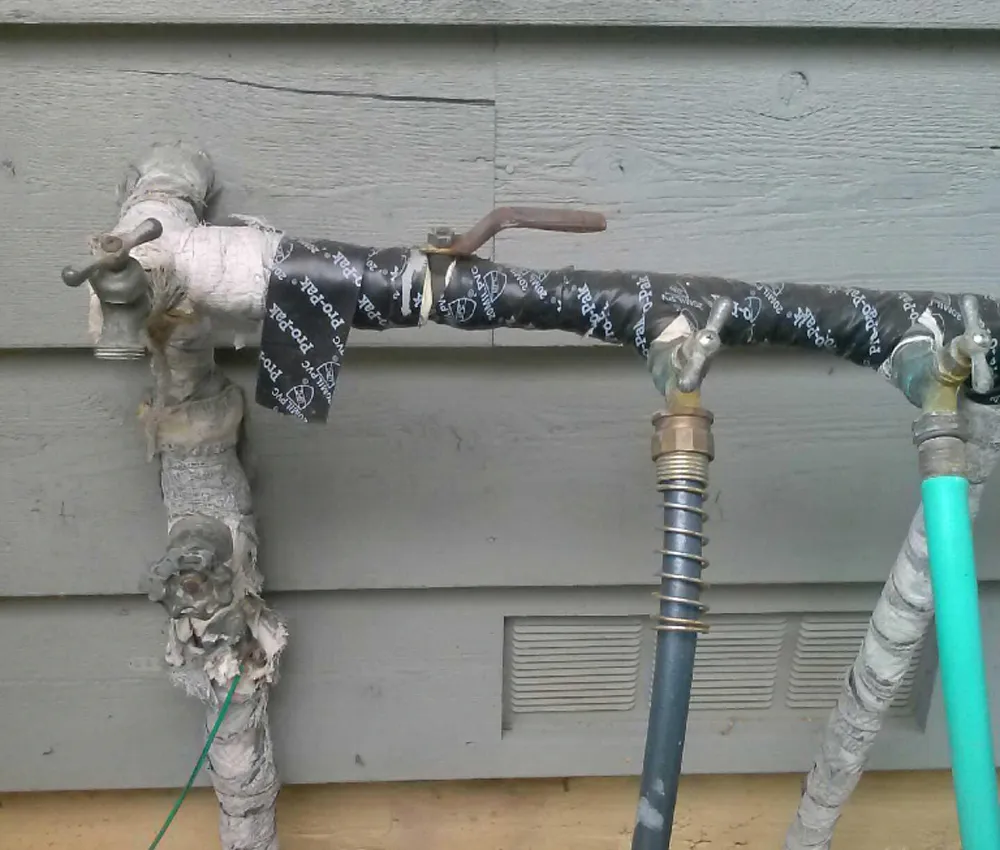 Insulated outdoor pipes with taps and hoses against a wooden wall. Insulated outdoor pipes with taps and hoses against a wooden wall.