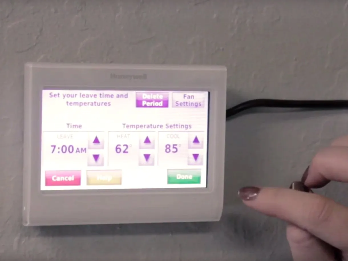  Close-up of a digital thermostat being adjusted by a person’s hand, displaying temperature settings for heat and cool.