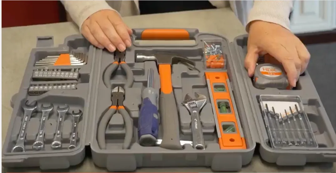 Open toolkit with various tools including pliers, wrenches, a hammer, screwdriver, level, tape measure, and drill bits on display. Hands are visible holding the case. Open toolkit with various tools including pliers, wrenches, a hammer, screwdriver, level, tape measure, and drill bits on display. Hands are visible holding the case.