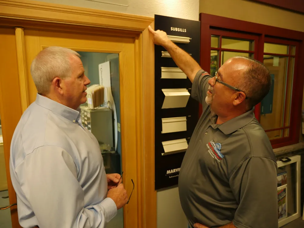 Two people discuss subsill samples on a display board inside a showroom. One person points to the samples while the other listens attentively. Two people discuss subsill samples on a display board inside a showroom. One person points to the samples while the other listens attentively.