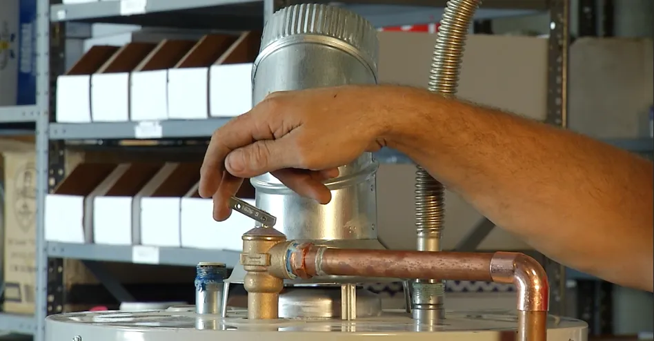 Close-up of a hand adjusting a valve on a water heater with shelving in the background. Close-up of a hand adjusting a valve on a water heater with shelving in the background.