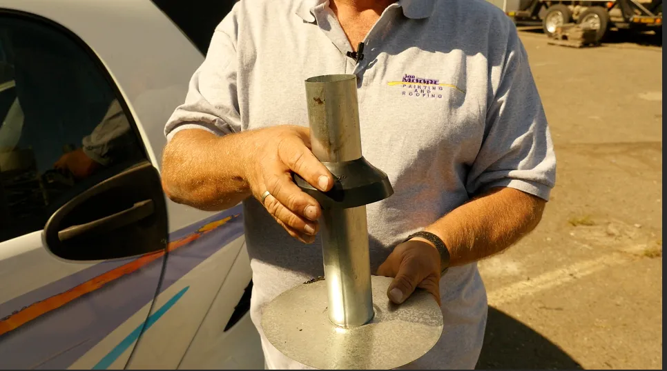 Person in a Joe Moore Painting & Roofing shirt holding a metal roofing component with a rubber seal, standing next to a vehicle. Person in a Joe Moore Painting & Roofing shirt holding a metal roofing component with a rubber seal, standing next to a vehicle.