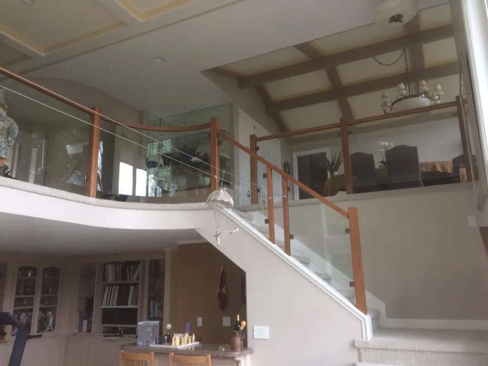 Indoor staircase with glass and wood balustrades connecting two floors. Upper floor features dining area, while lower floor has built-in shelves and a small table setup. Indoor staircase with glass and wood balustrades connecting two floors. Upper floor features dining area, while lower floor has built-in shelves and a small table setup.