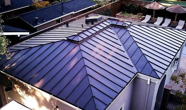 Aerial view of a house with a newly installed metal roof, featuring clean lines and precise seams under clear weather. Aerial view of a house with a newly installed metal roof, featuring clean lines and precise seams under clear weather.