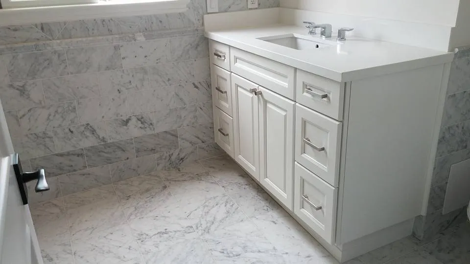 A bathroom with marble tile walls and floor, featuring a white vanity cabinet with silver handles and a modern faucet. A bathroom with marble tile walls and floor, featuring a white vanity cabinet with silver handles and a modern faucet.