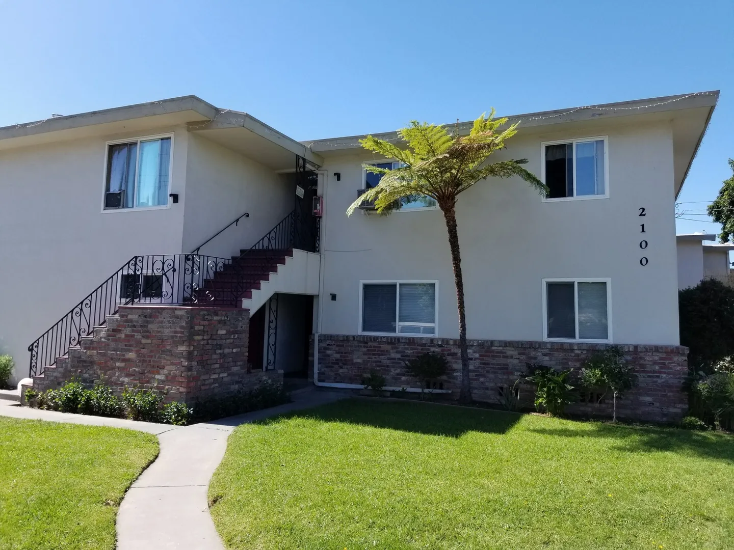  Two-story building with white walls, large windows, a tree in front, and an exterior staircase leading to the second floor.