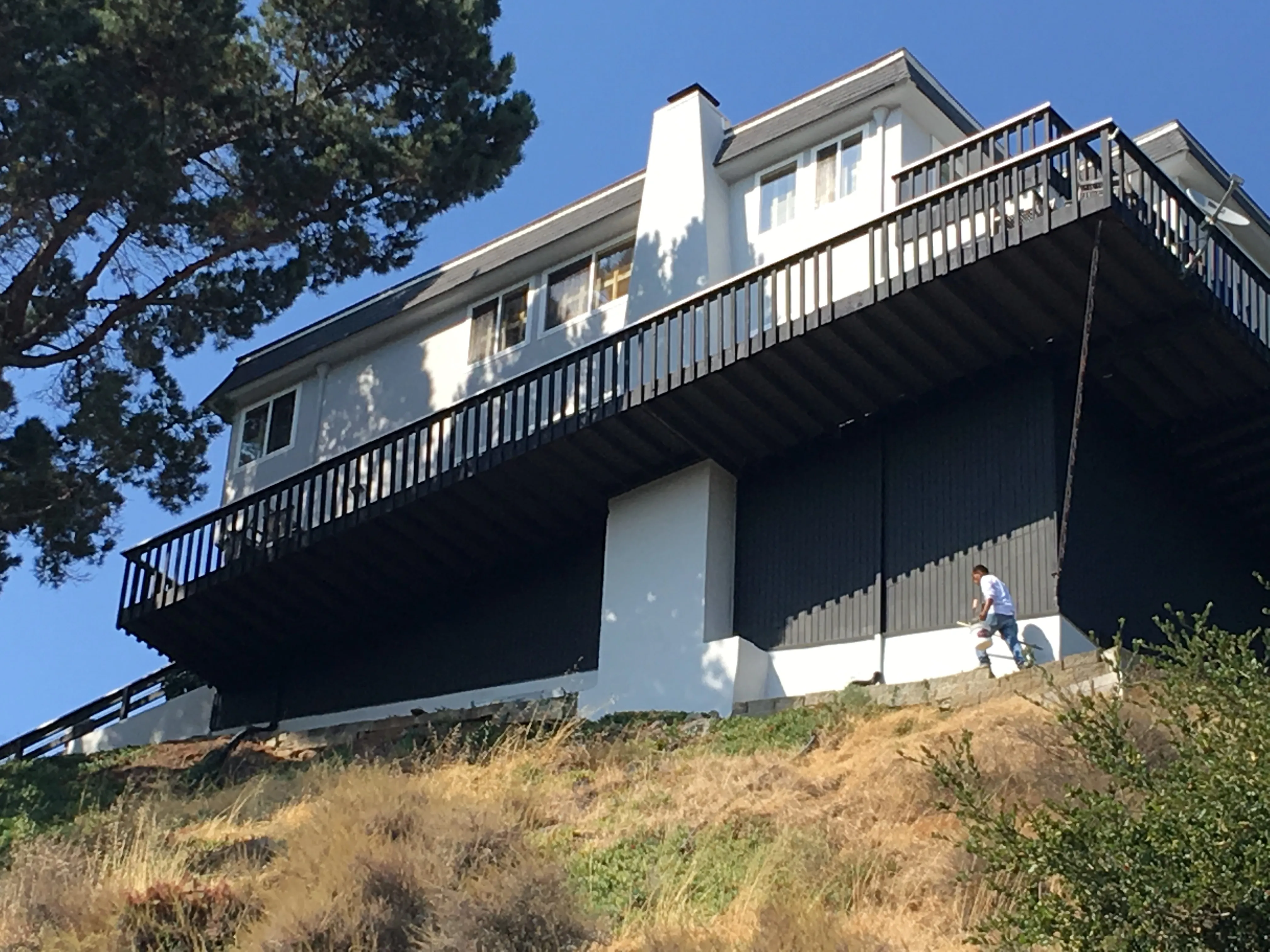 Picture of  A dedicated worker applies paint to the foundation of a hillside home, ensuring a precise finish. This meticulous care highlights S & S Painting and Coatings, Inc.'s focus on quality outcomes. Copyright ©2025 Diamond Certified Resource.

 - S & S Painting and Coatings, Inc.