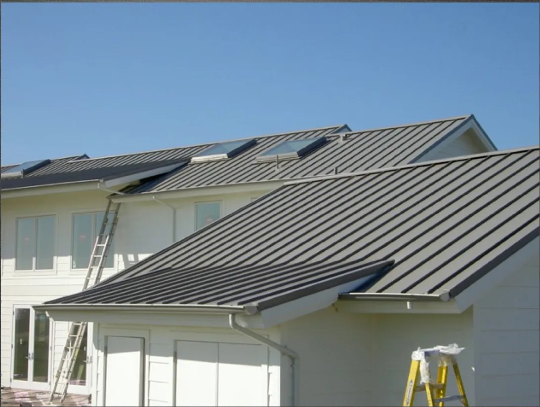 A metal roof on a building with multiple skylights, ladders are propped against the walls, under a clear blue sky. A metal roof on a building with multiple skylights, ladders are propped against the walls, under a clear blue sky.