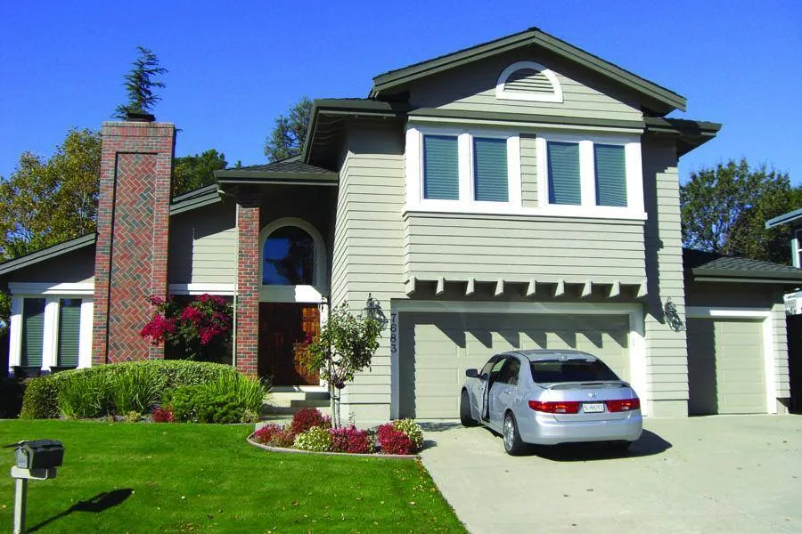 Two-story house with gray siding and a brick chimney, a neatly manicured lawn, and a silver car in the driveway. Two-story house with gray siding and a brick chimney, a neatly manicured lawn, and a silver car in the driveway.