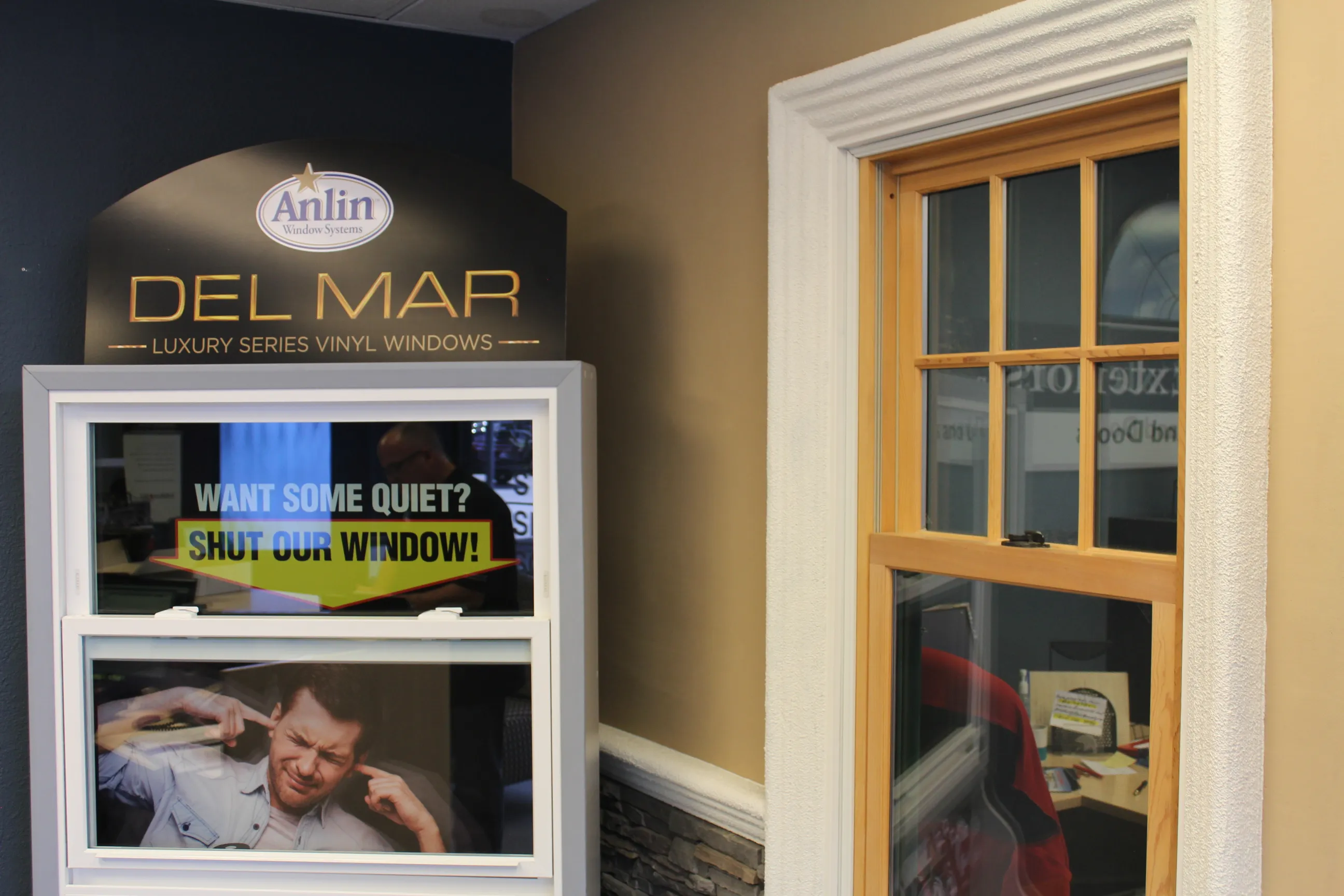 Display of Del Mar luxury series vinyl windows with a sign reading "Want some quiet? Shut our window!" and a nearby window frame. Display of Del Mar luxury series vinyl windows with a sign reading "Want some quiet? Shut our window!" and a nearby window frame.
