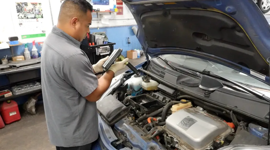 Technician inspecting an engine component in an auto repair shop with the hood of a car open. Tools and supplies are visible in the background. Technician inspecting an engine component in an auto repair shop with the hood of a car open. Tools and supplies are visible in the background.