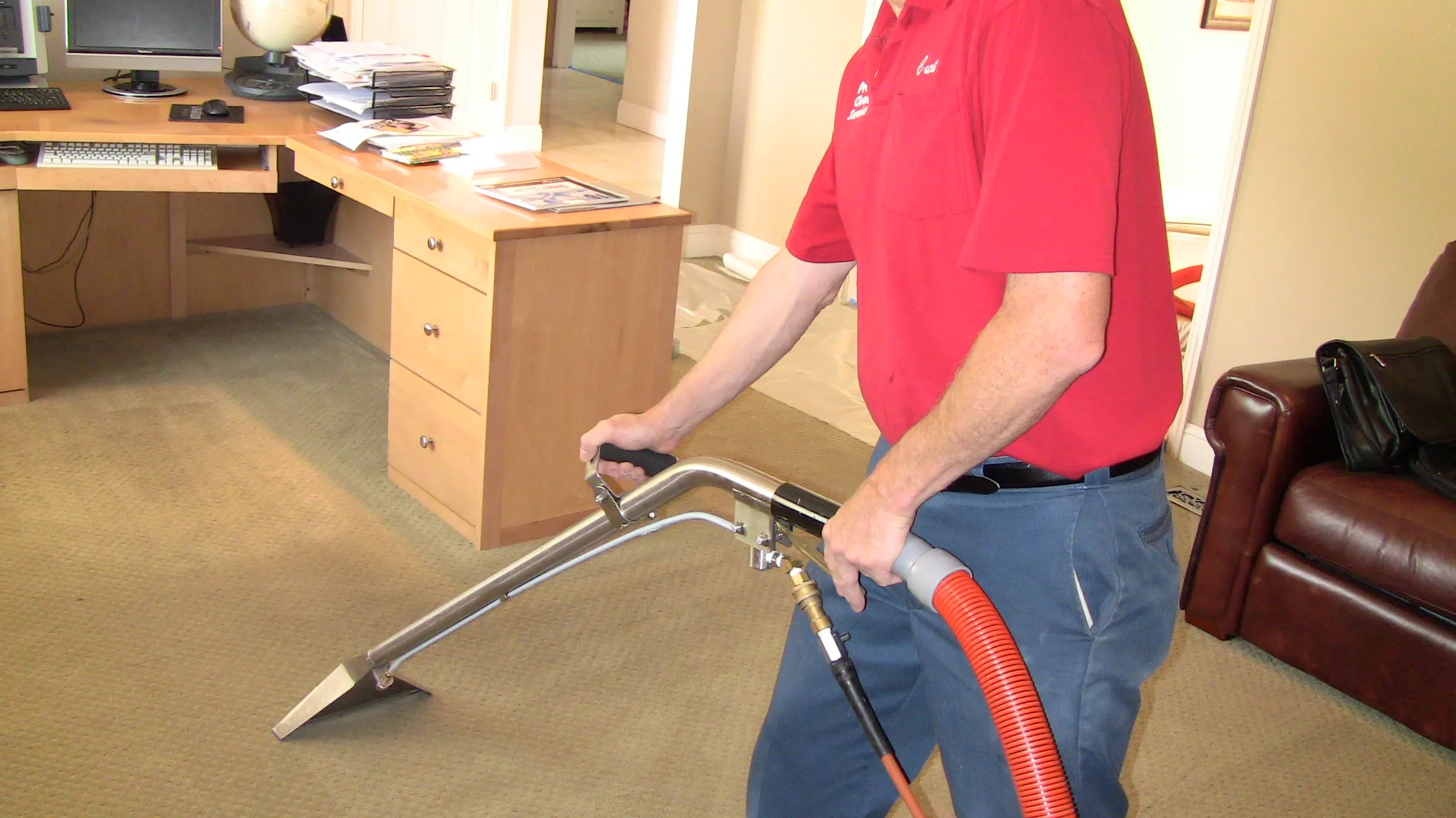 A person in a red shirt uses a carpet cleaning machine on an office carpet, surrounded by a desk, chair, and papers. A person in a red shirt uses a carpet cleaning machine on an office carpet, surrounded by a desk, chair, and papers.
