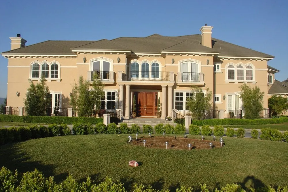  A grand beige mansion with arched windows and a neatly trimmed lawn under a clear blue sky.