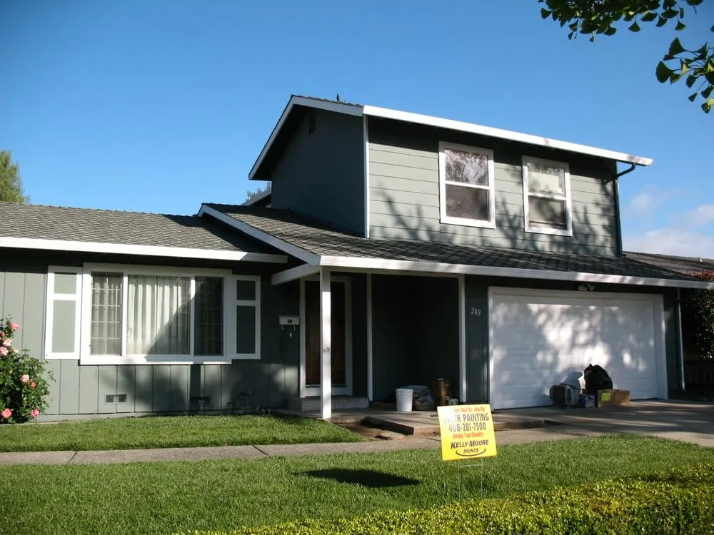 A two-story house with a fresh gray exterior paint job, a Faith Painting sign on the lawn, and various painting tools near the garage.