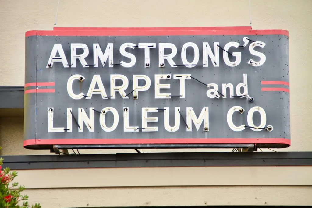 A vintage neon sign for Armstrong Carpet & Linoleum Co., featuring white letters on a dark background with red accents. A vintage neon sign for Armstrong Carpet & Linoleum Co., featuring white letters on a dark background with red accents.