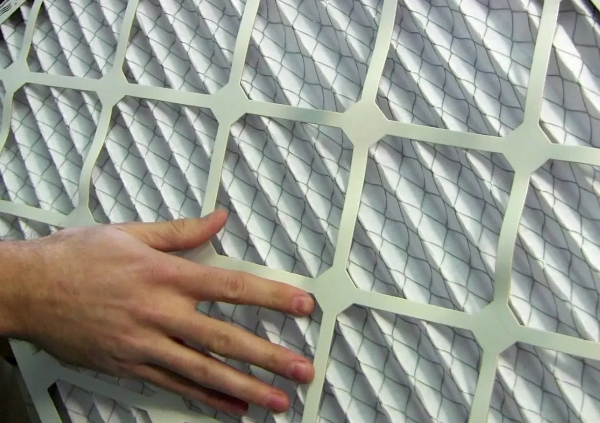  A close-up of a hand touching a white air filter with a wire mesh pattern, showcasing detailed inspection work.