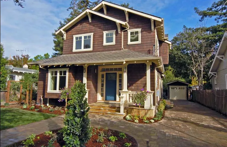 A two-story house with a brown wooden exterior, white trim, and a blue front door, surrounded by a landscaped garden and driveway. A two-story house with a brown wooden exterior, white trim, and a blue front door, surrounded by a landscaped garden and driveway.