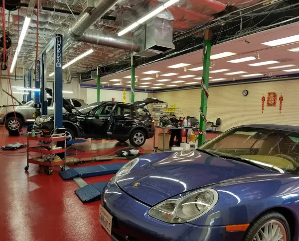  Interior of an auto repair shop with a blue sports car and a black SUV on lifts, surrounded by tools and equipment.