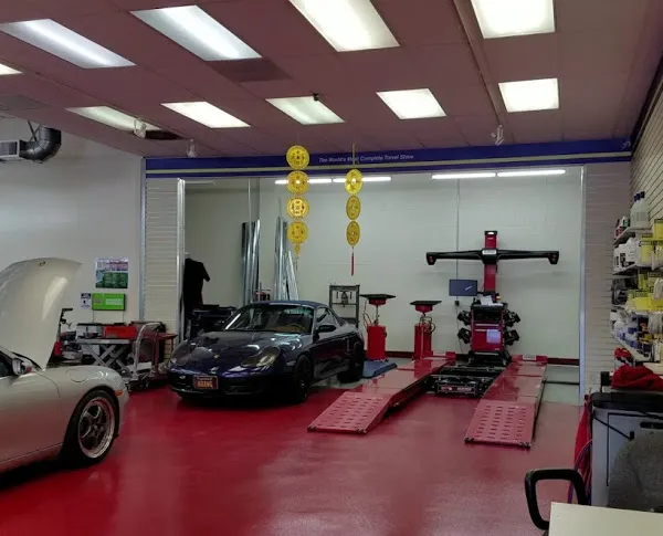  Auto repair shop with black car on red flooring, open hood of another car, tools, and car lift visible.