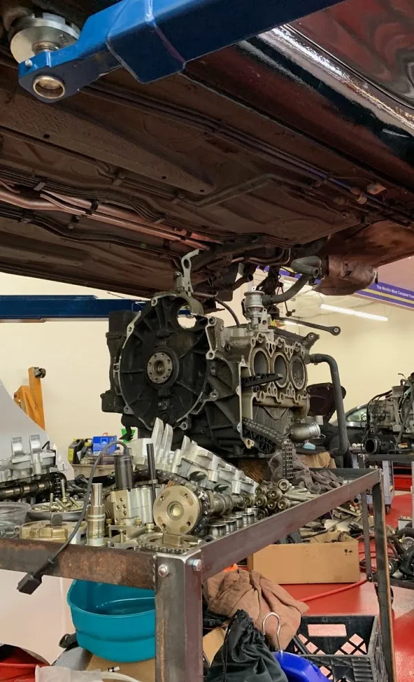 A disassembled vehicle engine on a workshop bench surrounded by various engine parts and tools in an auto repair shop.