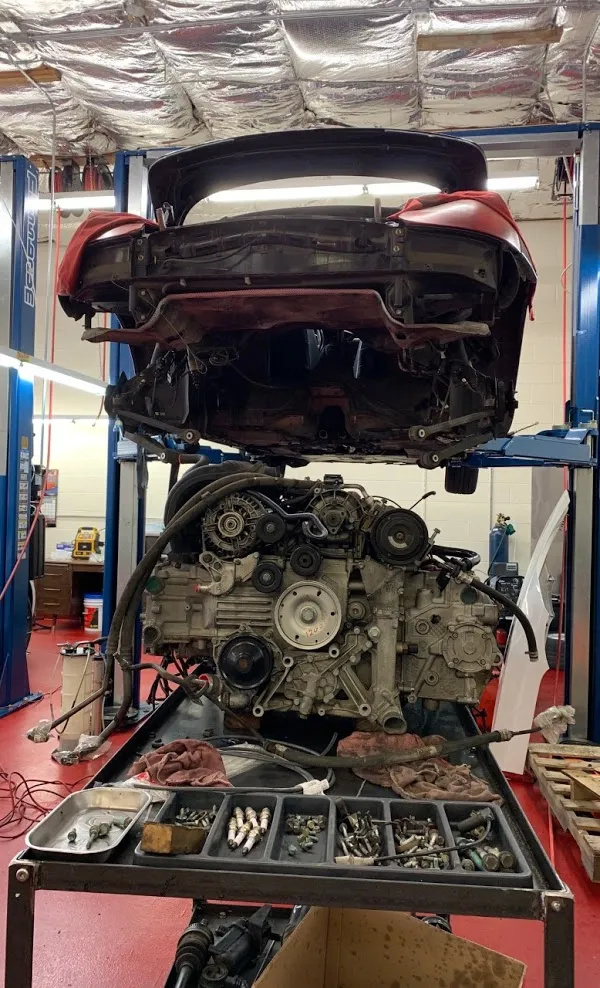  A car is lifted on a mechanic's lift, with its engine removed and placed on a cart below. Various tools and parts are organized on the cart.