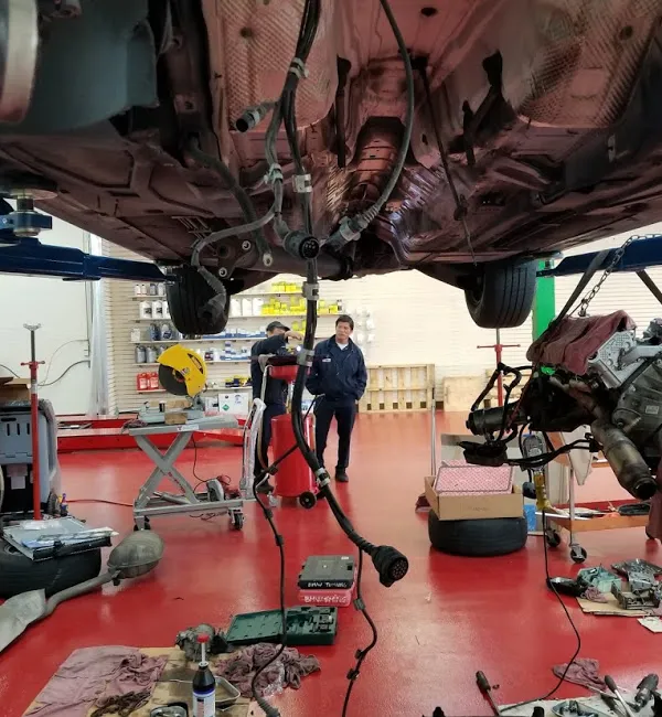  Mechanics work under a raised car, with parts and tools scattered around a clean auto repair garage, highlighting detailed maintenance work.