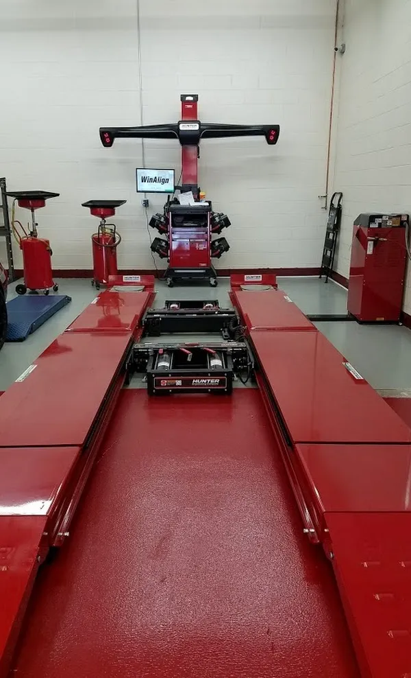  Red vehicle alignment machine in a clean auto repair shop, with various tools and equipment nearby.
