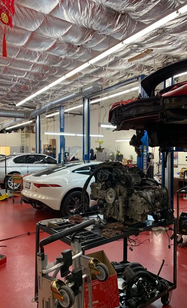   
Auto repair shop interior with cars on lifts, a detached engine on a cart, and various tools and equipment in a brightly lit workspace.