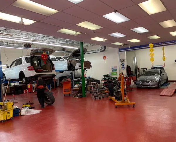   
Auto repair shop with cars on lifts, a technician managing a tire, and organized tools on red floor.