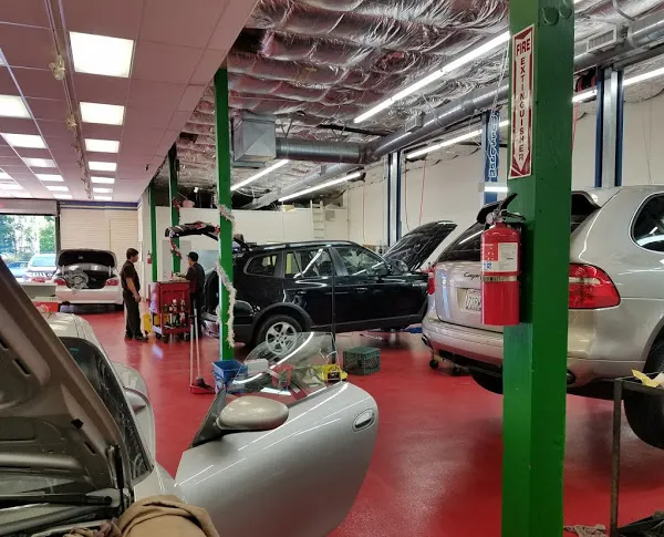  Inside an auto repair shop with red floors, multiple cars are being serviced by technicians with tools and equipment.