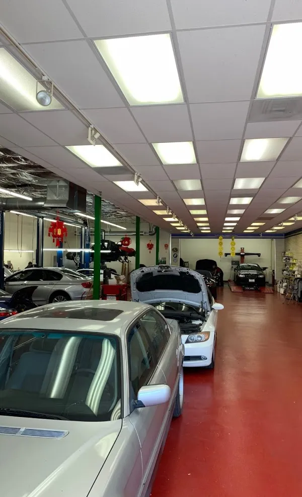  Interior of an auto repair shop with several cars lined up on a red floor, some with open hoods, under bright overhead lighting.