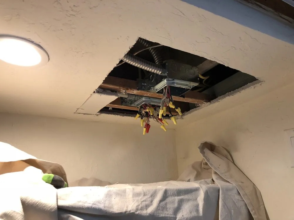  Ceiling with a cutout exposing electrical wiring and a junction box, surrounded by protective coverings.
