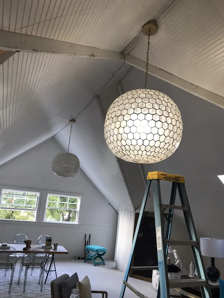 Interior view of an attic with a hexagonal-patterned pendant light, ladder, and two windows overlooking greenery.