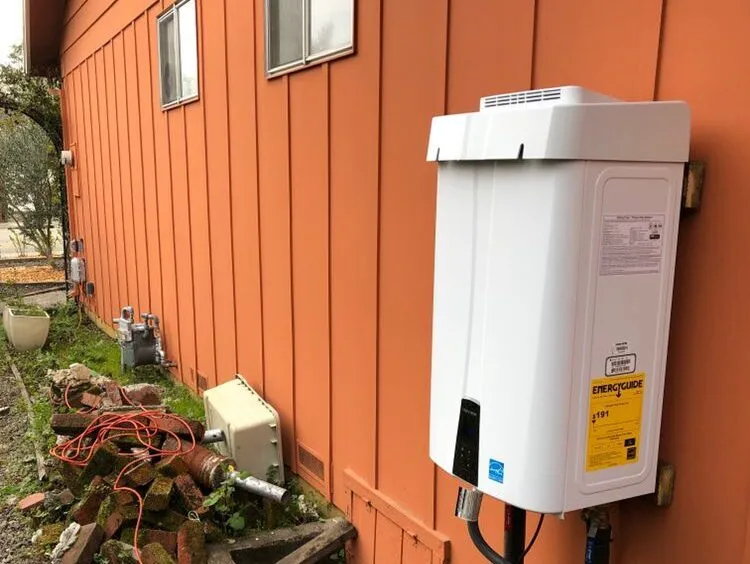 Tankless water heater mounted on an orange wall next to some cables and bricks. Tankless water heater mounted on an orange wall next to some cables and bricks.