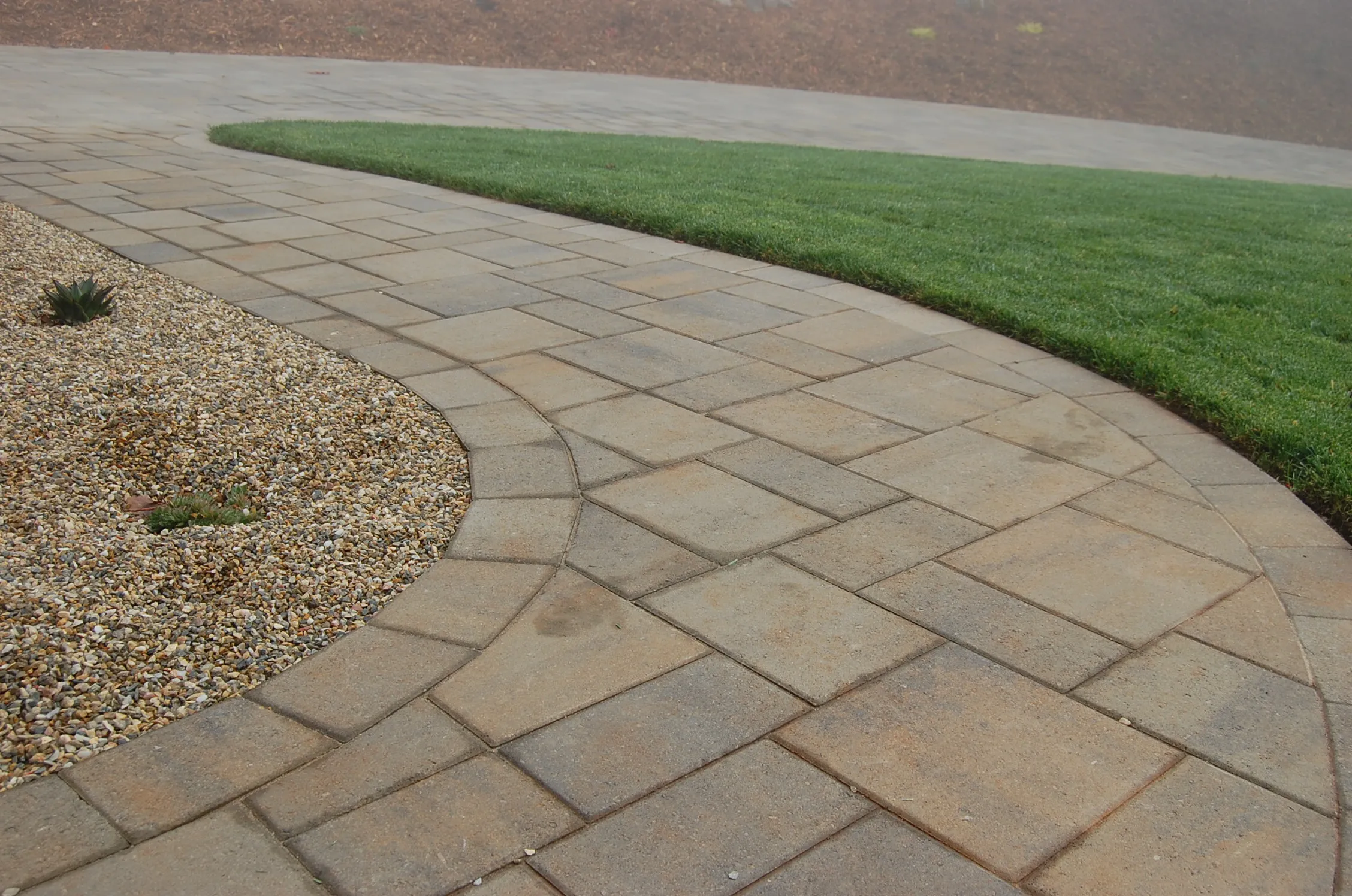 Picture of Curving elegantly, the stone paver path by The Legacy Paver Group seamlessly divides lush grass and a pebbled area, showcasing their focus on quality outcomes. The company's expertise is reflected in every detail. Copyright ©2025 Diamond Certified Resource

 - The Legacy Paver Group